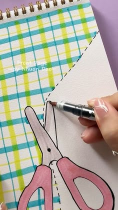 a person is holding a pen and drawing on a piece of paper with scissors in it