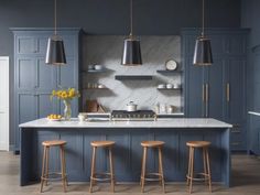 a kitchen with blue cabinets and stools in the center, two hanging lights above the island