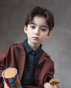 a young boy in a brown coat holding a peanut butter sandwich and a can of cereal