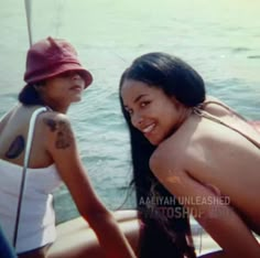 two young women sitting next to each other in the water, one wearing a red hat