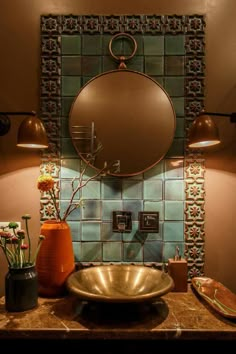 a bathroom sink sitting under a round mirror next to a vase with flowers in it