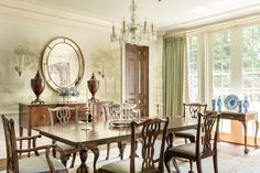 a dining room table and chairs in front of a large window with an oval mirror on the wall