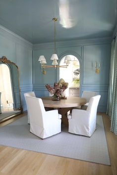 a dining room with blue walls and white chairs around a round wooden table in the center