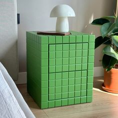 a green box sitting on top of a wooden floor next to a lamp and potted plant