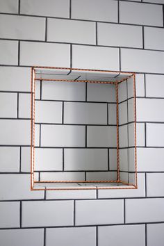 a square mirror mounted to the side of a white brick wall with an orange wire frame