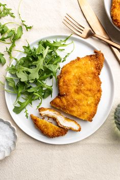 a white plate topped with fried chicken next to green vegetables and utensils on top of a table