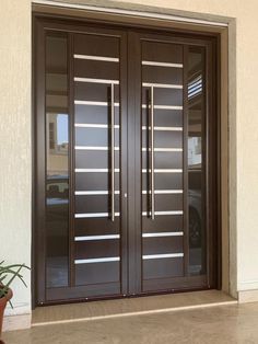 a pair of brown double doors in front of a white wall and potted plant