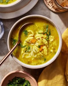 a bowl of soup with noodles, carrots and spinach in it next to other bowls