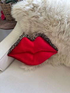 a white furry animal laying on top of a couch next to a red pillow and purse