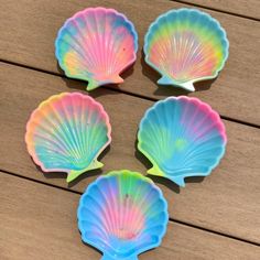 four colorful scallop shells sitting on top of a wooden table