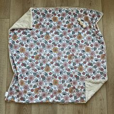 a white and brown flowered blanket laying on top of a wooden floor