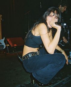 a woman sitting on top of a stool while holding a microphone to her mouth and singing into a mic