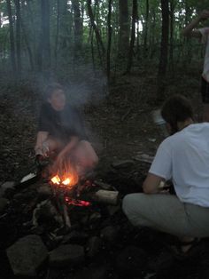 three people sitting around a campfire in the woods