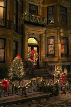 christmas lights decorate the front of an old building at night with trees and wreaths