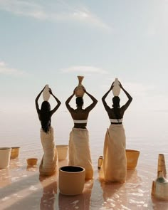 three women standing in the water with their hands on their hipss and holding pots