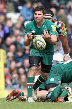 a rugby player holding the ball in his hands as he is surrounded by other players