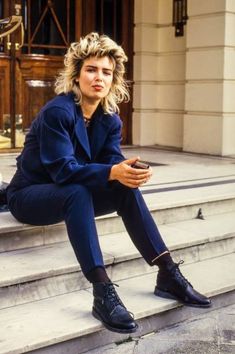 a woman sitting on the steps in front of a building looking at her cell phone