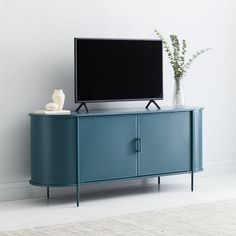 a flat screen tv sitting on top of a blue cabinet next to a vase with a plant