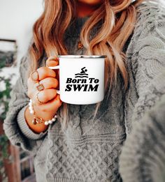 a woman holding a coffee mug with the words born to swim printed on it in front of her face