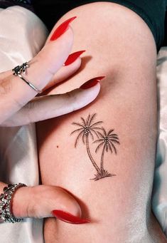 a woman with red nail polish on her nails and a palm tree tattoo on her thigh