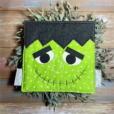 a close up of a green and black face on a piece of cloth with plants in the background