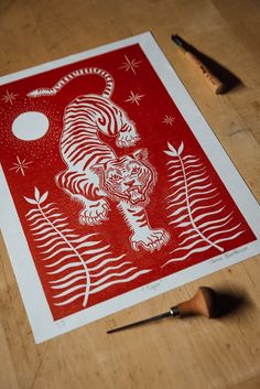 a red and white tiger print sitting on top of a wooden table next to a pair of scissors