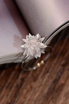 an open book sitting on top of a wooden table next to a flower shaped ring