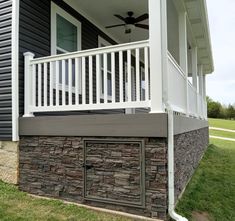 a porch with a stone wall and white railing on the side of it, next to a house