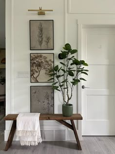 a wooden bench sitting in front of a white wall with pictures on the wall above it