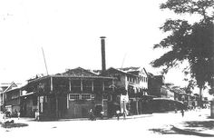 an old black and white photo of people walking in front of a building with a chimney