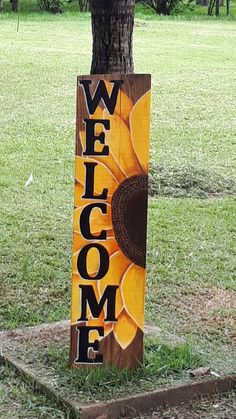 a wooden welcome sign with a sunflower painted on the front and side, next to a tree