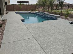 a small pool in the middle of a backyard with rocks and gravel around it, surrounded by a fence