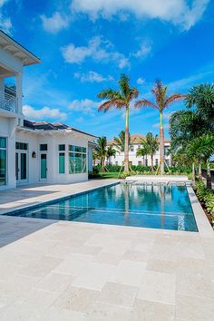 a large swimming pool in front of a white house with palm trees on the side