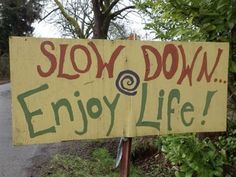 a sign that says slow down enjoy life on the side of a road with trees in the background