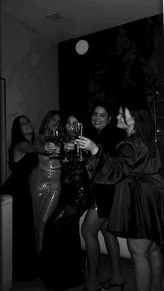 some women are standing together and drinking wine in black and white photo with lights on the wall behind them