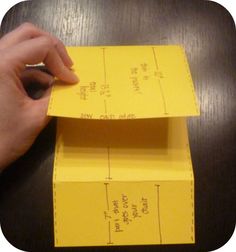 a hand is holding a piece of yellow paper on top of a wooden table with measurements