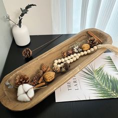 a wooden tray with pine cones, nuts and other things in it on a table