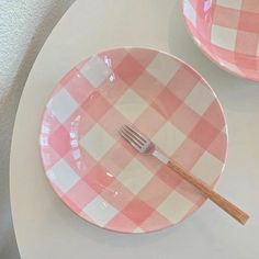 two pink and white checkered plates with a fork in the middle on a table