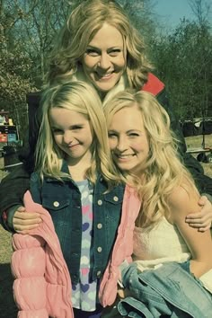 three girls are posing for the camera with their arms around each other and one girl is wearing a pink jacket