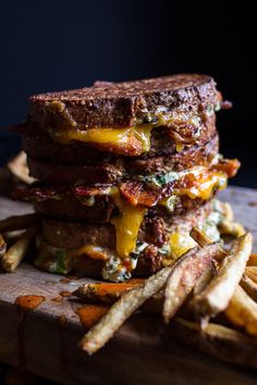 a stack of grilled cheese and bacon sandwiches next to french fries on a cutting board