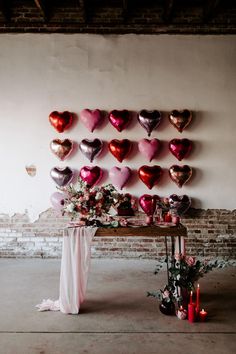 a table topped with lots of heart shaped balloons next to a wall filled with flowers and candles