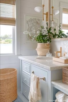 a bathroom with white cabinets and marble counter tops, plants in baskets on the vanity