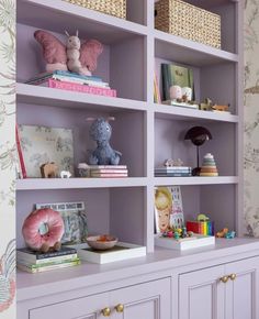 the shelves are filled with books, toys and stuffed animals in pastel purples