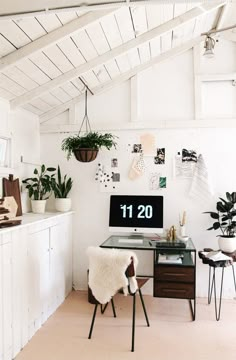 a desk with a computer on top of it next to a chair and potted plants