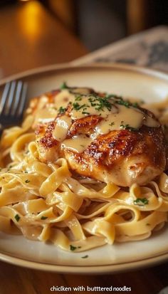 chicken with buttered noodles on a plate next to a fork and glass of wine