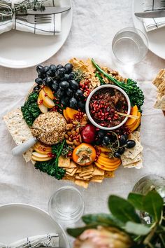 a platter filled with fruit and crackers on top of a white table cloth