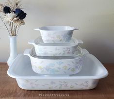 a stack of white dishes sitting on top of a wooden table next to a vase with flowers