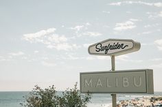 a sign that is on top of a pole next to the ocean with people in the background