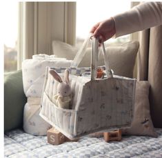 a person holding a bag with a stuffed animal in it on top of a bed