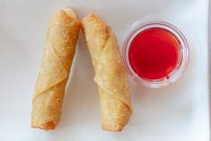 two pastries on a white plate next to a cup of red liquid and sauce